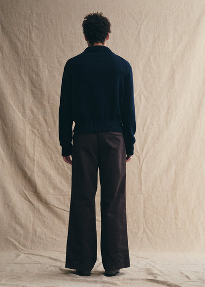 Person wearing a dark sweater and brown pants standing against a beige backdrop