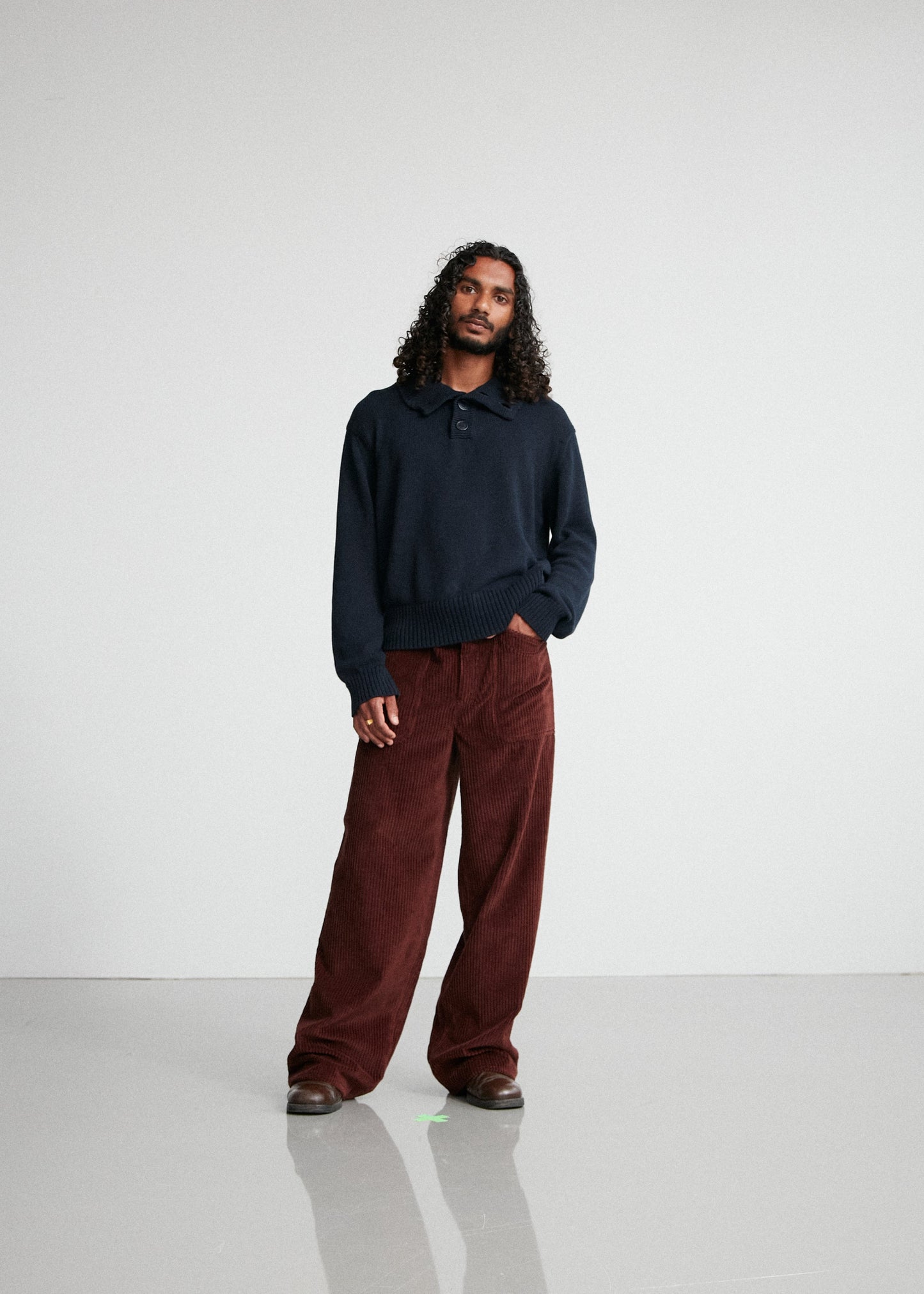Man wearing a dark sweater and brown pants standing against a white background