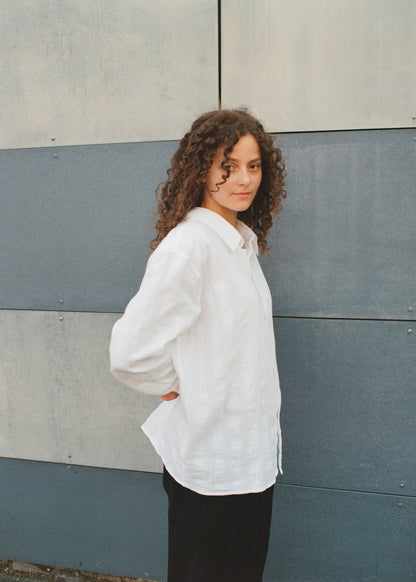 Person wearing a white shirt standing against a gray wall