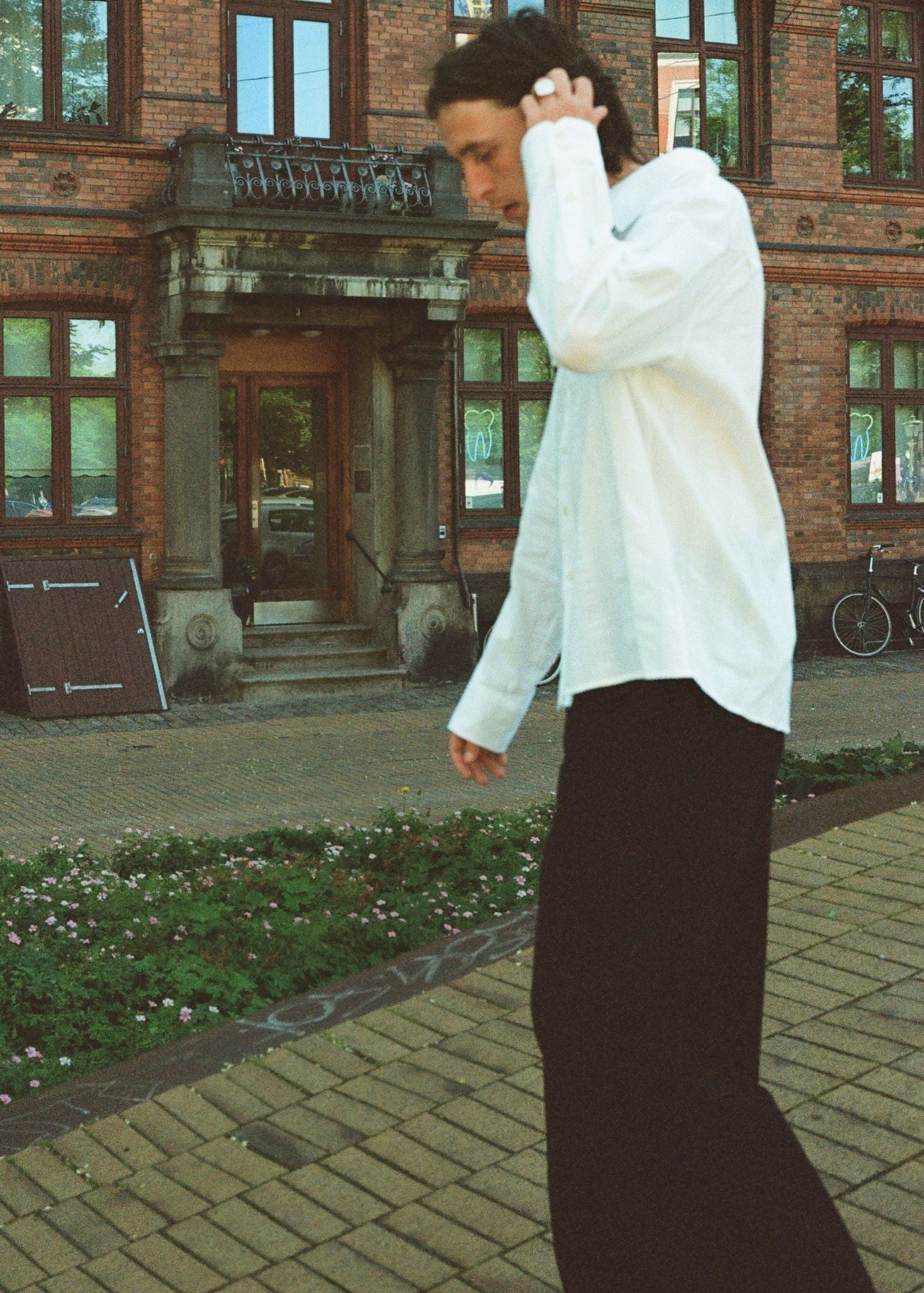 Person in a white shirt and black pants standing on a sidewalk with a brick building in the background