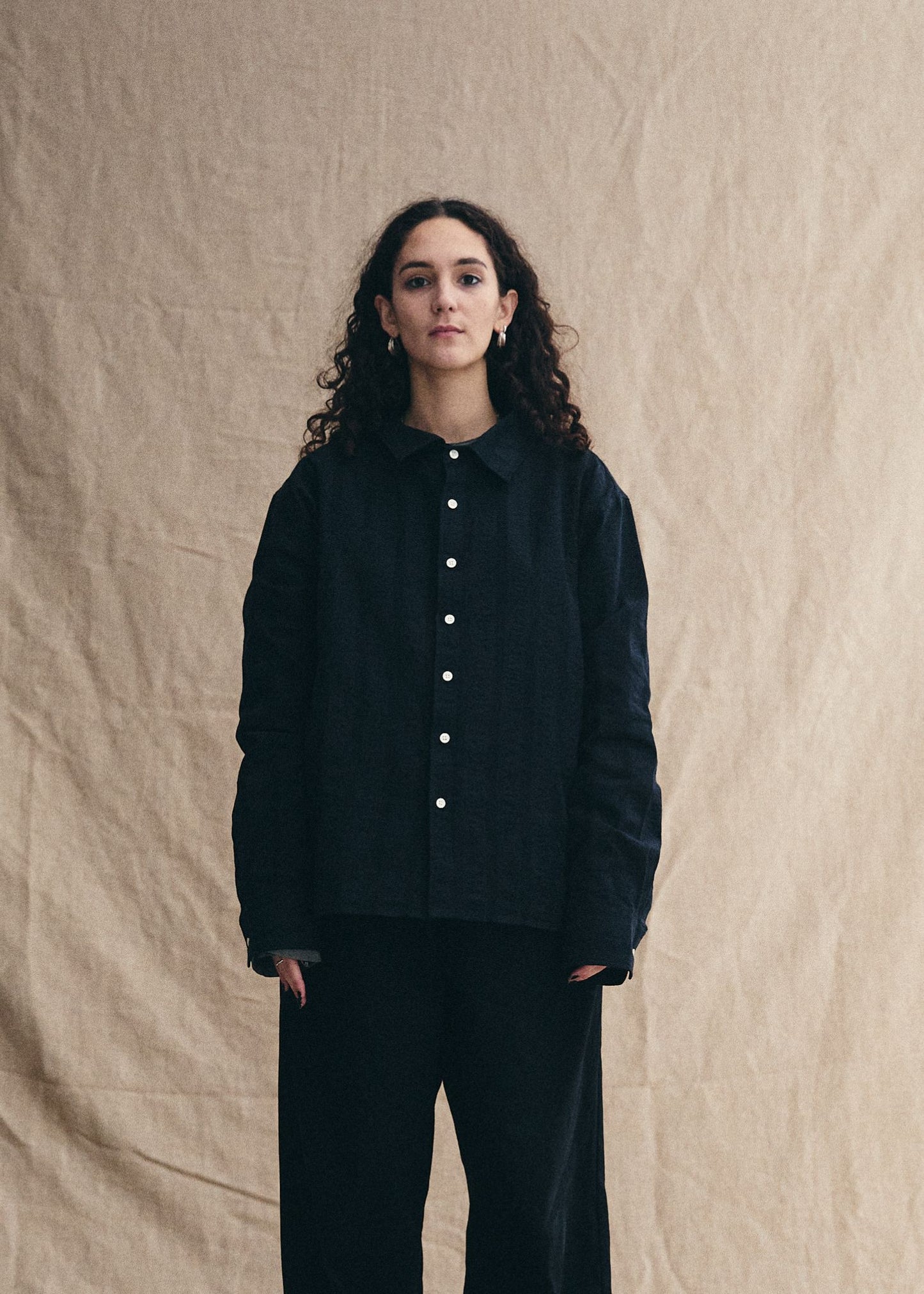 Person wearing a black jacket with white buttons against a beige background