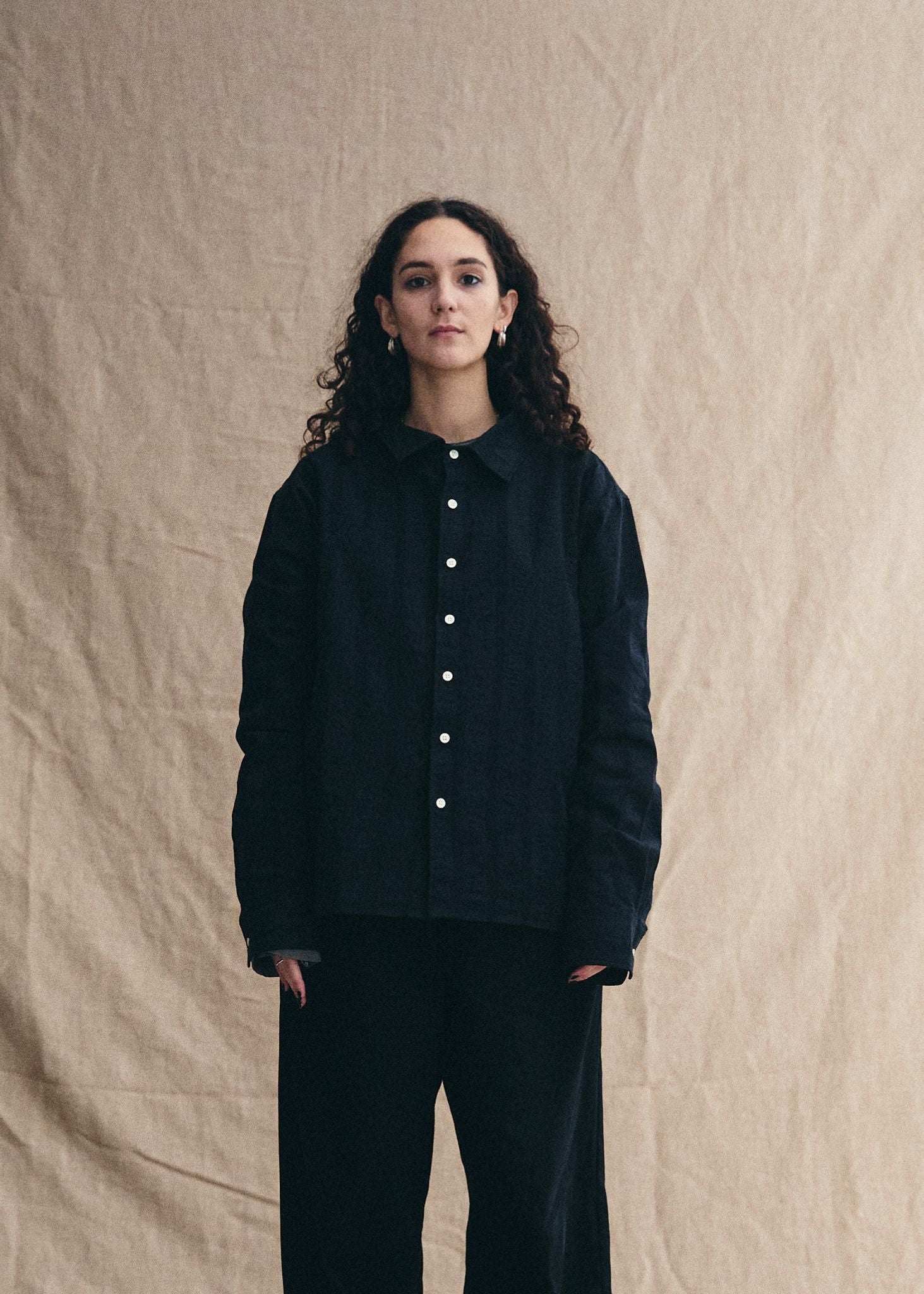 Person wearing a black jacket with white buttons against a beige background