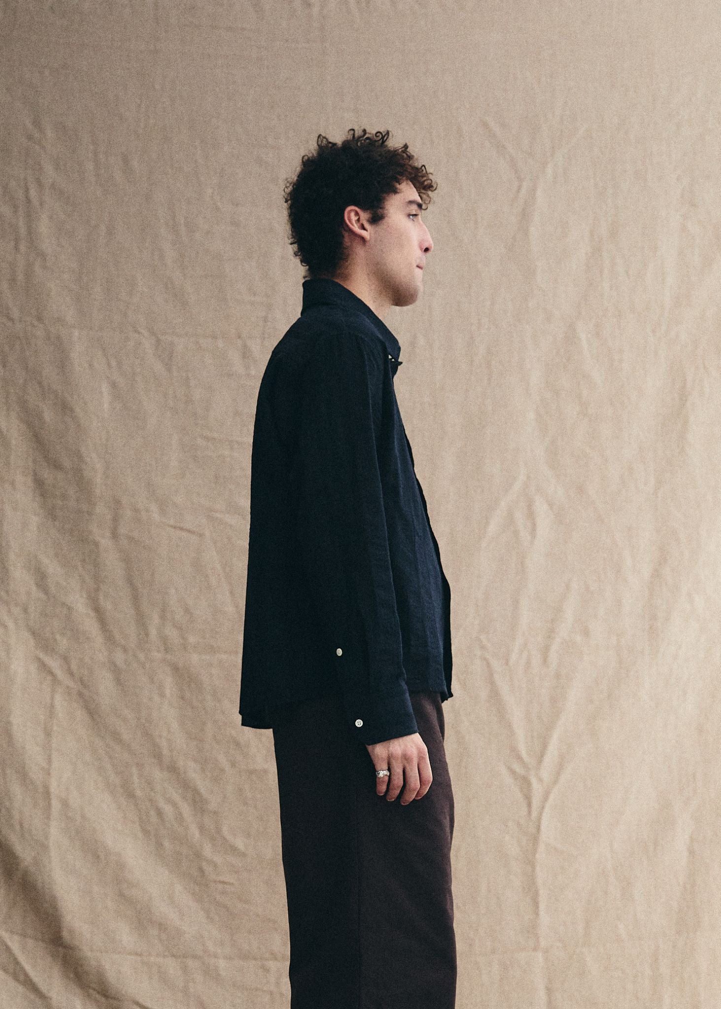 Man wearing a dark jacket and pants standing against a beige textured wall