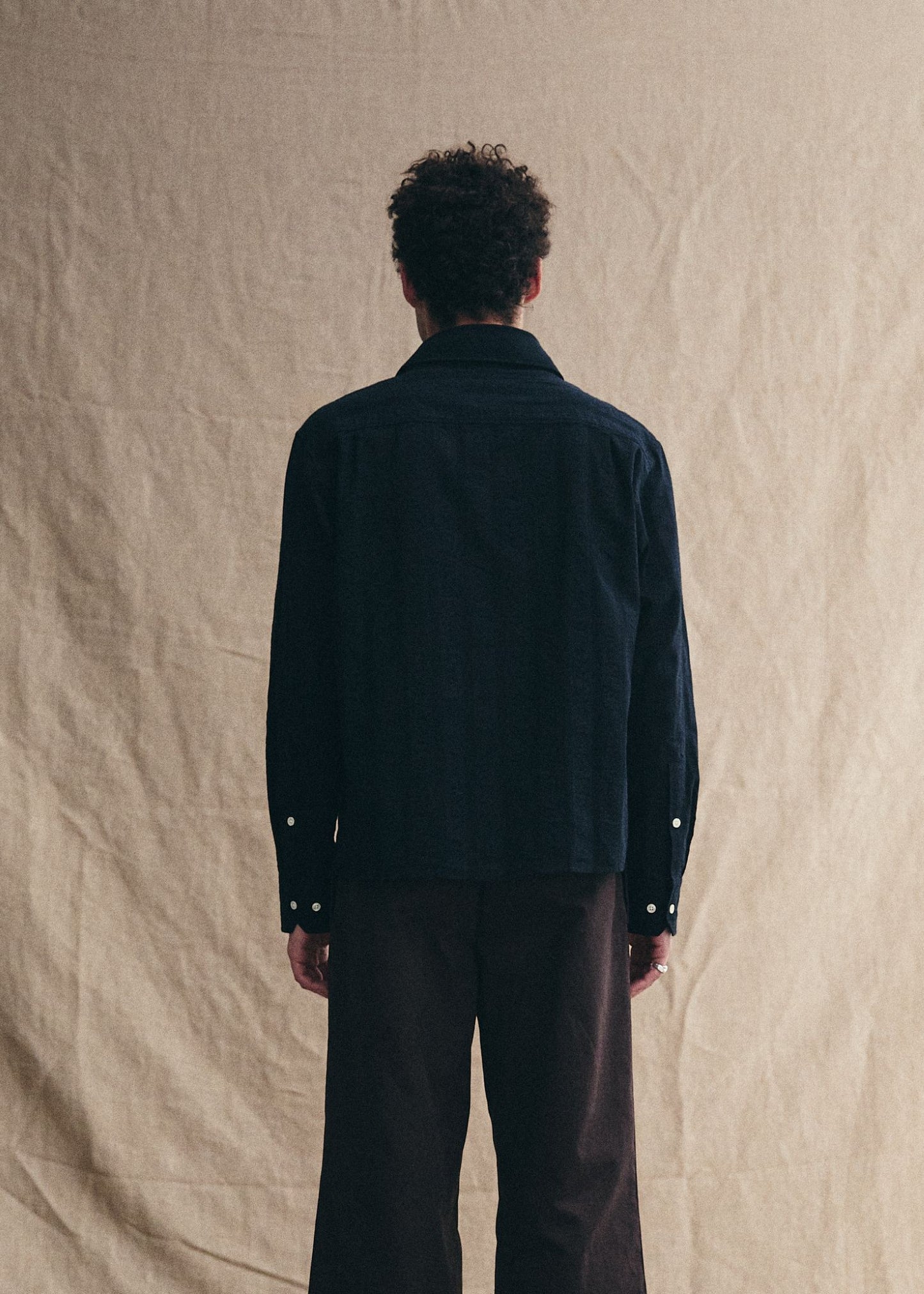 Person wearing a dark jacket and pants against a beige background