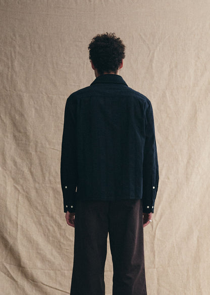 Person wearing a dark jacket and pants against a beige background