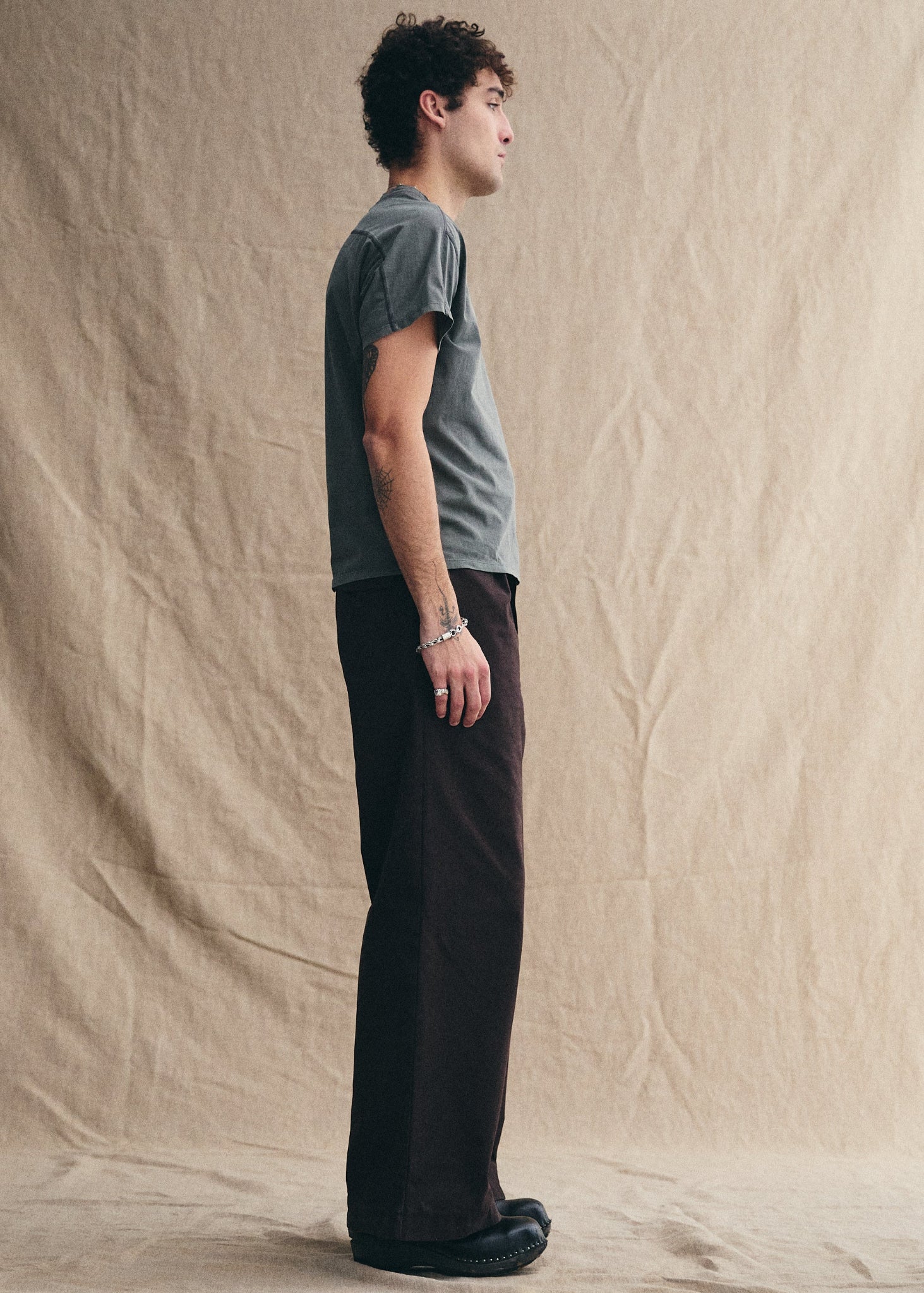 Person wearing a gray t-shirt and dark pants standing against a beige backdrop