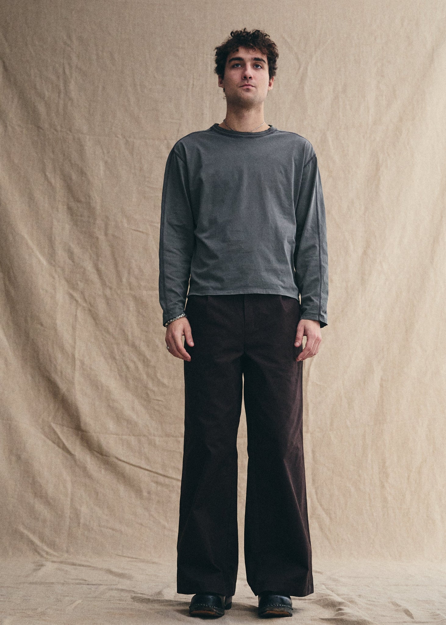 Man wearing a gray long-sleeve shirt and black pants against a beige background