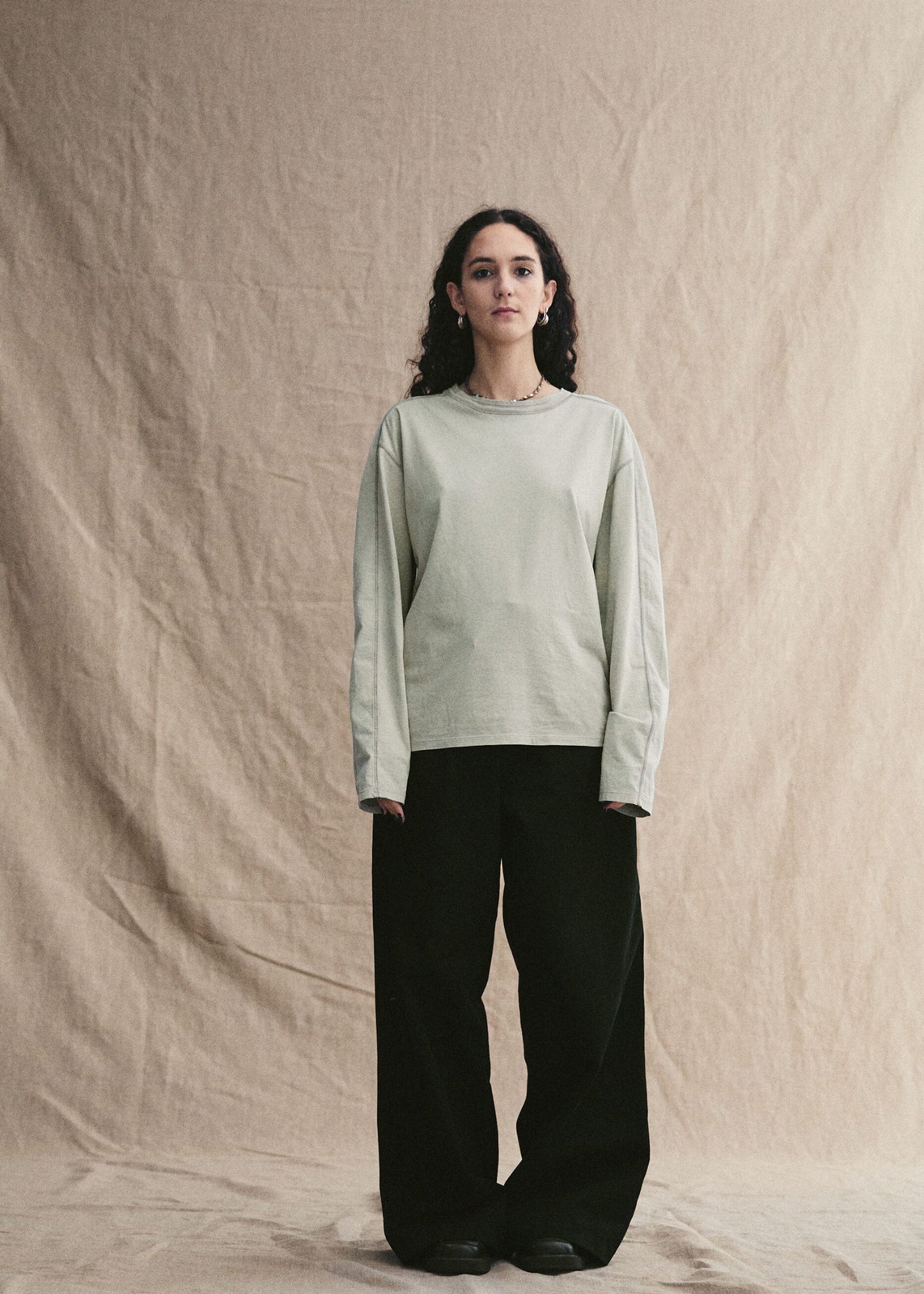 Woman wearing a light green sweater and black pants against a beige background