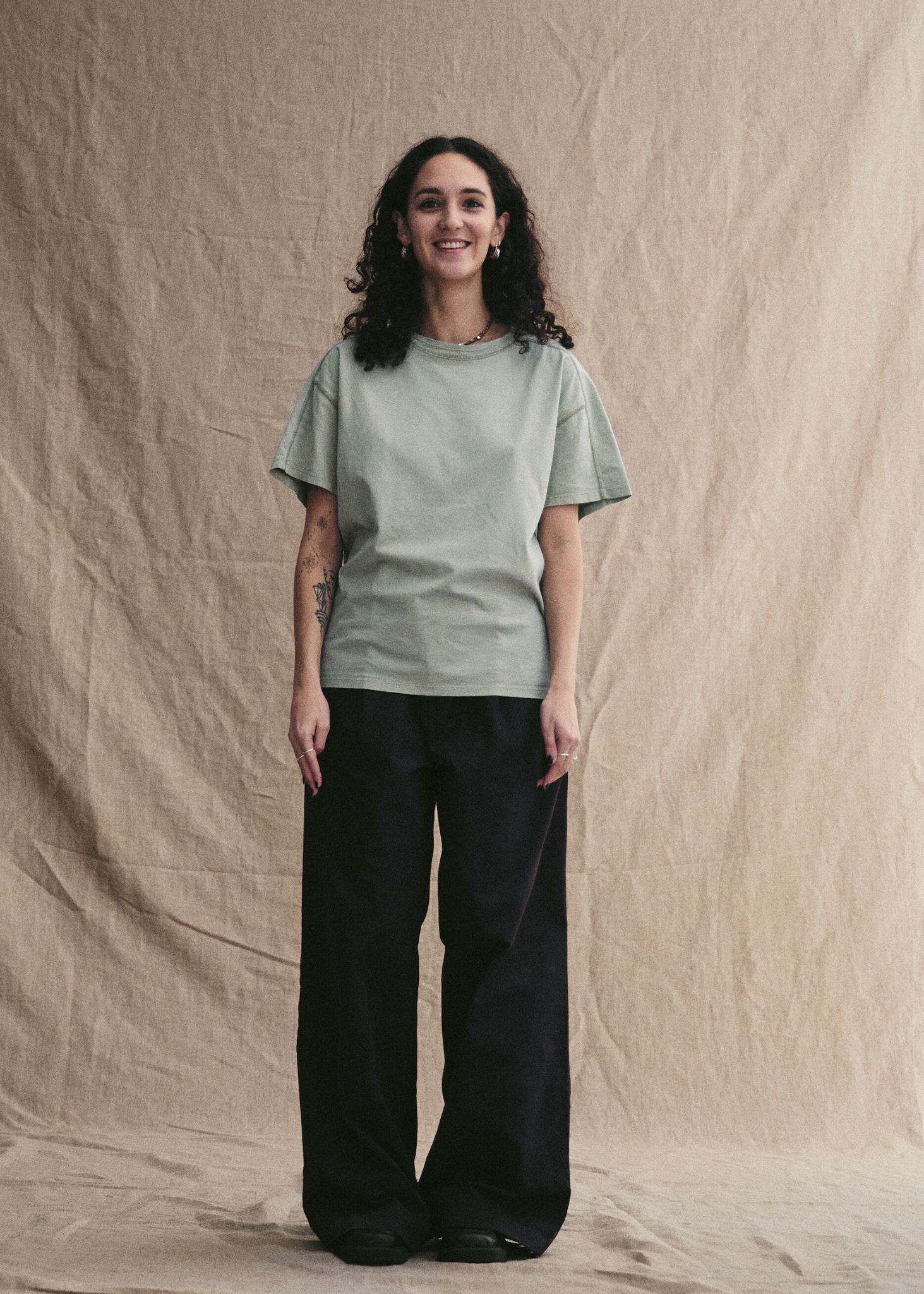 Woman wearing a light green t-shirt and black pants against a beige background